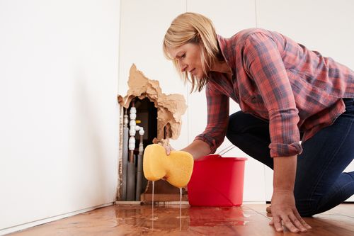 Image is of a woman cleaning up water leak concept of Boca Raton residential plumbing
