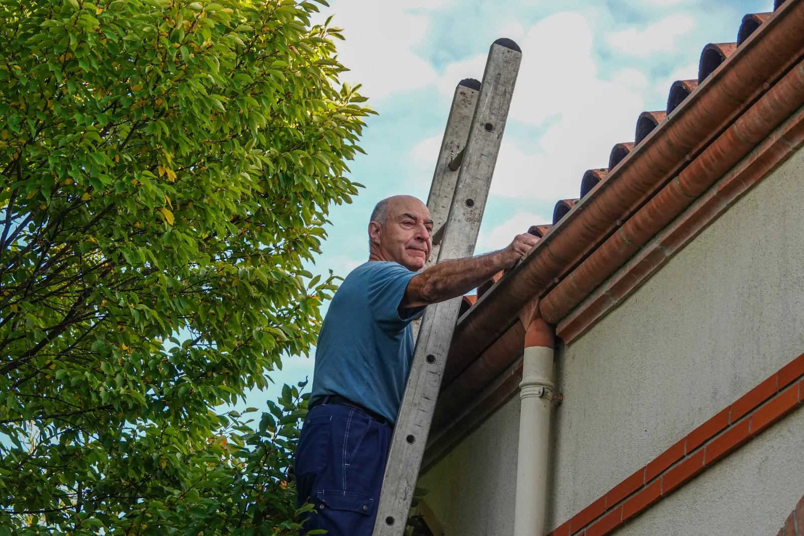 Man on ladder inspecting his gutters before a storm